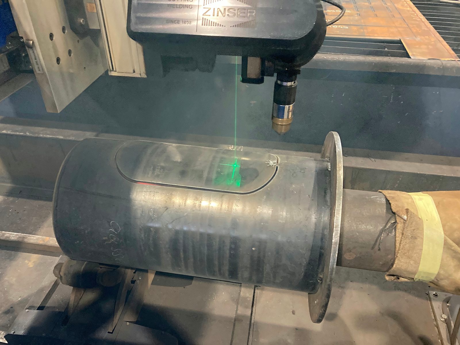 Torche plasma avec laser de positionnement vert au-dessus d'un tube en acier dont la paroi porte déjà une lumière oblongue