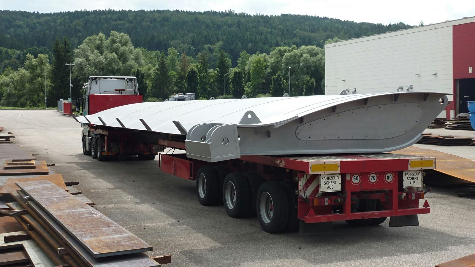Metallkonstruktion från den kompletta tillverkningen — svetsad stålkomponent på trailern, lastad framför verkstadshallen för tungtransport